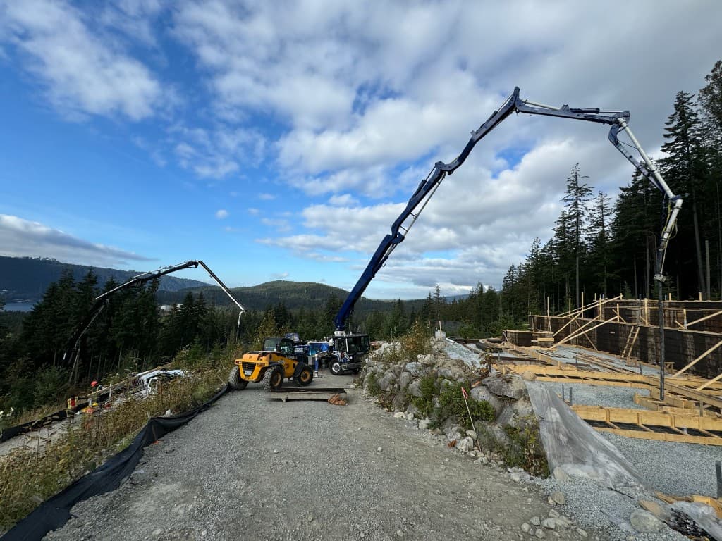 Multi-family development site with concrete pump truck and foundation formwork against a forested hillside