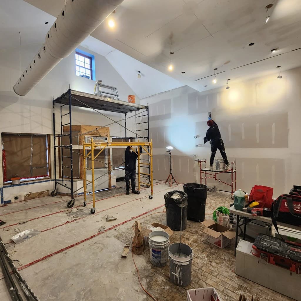 Commercial restaurant interior under construction with drywall, scaffolding, and workers finishing walls