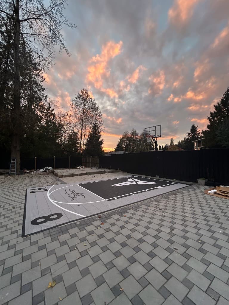 Custom backyard basketball half-court with modular surfacing and patio pavers at sunset